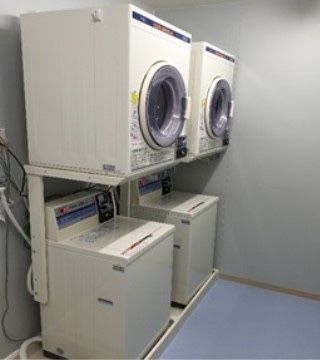 洗濯室である。カード式の洗濯機と乾燥機が壁沿いにそれぞれ二機設置されている。床にはブルーのシートが敷かれている。