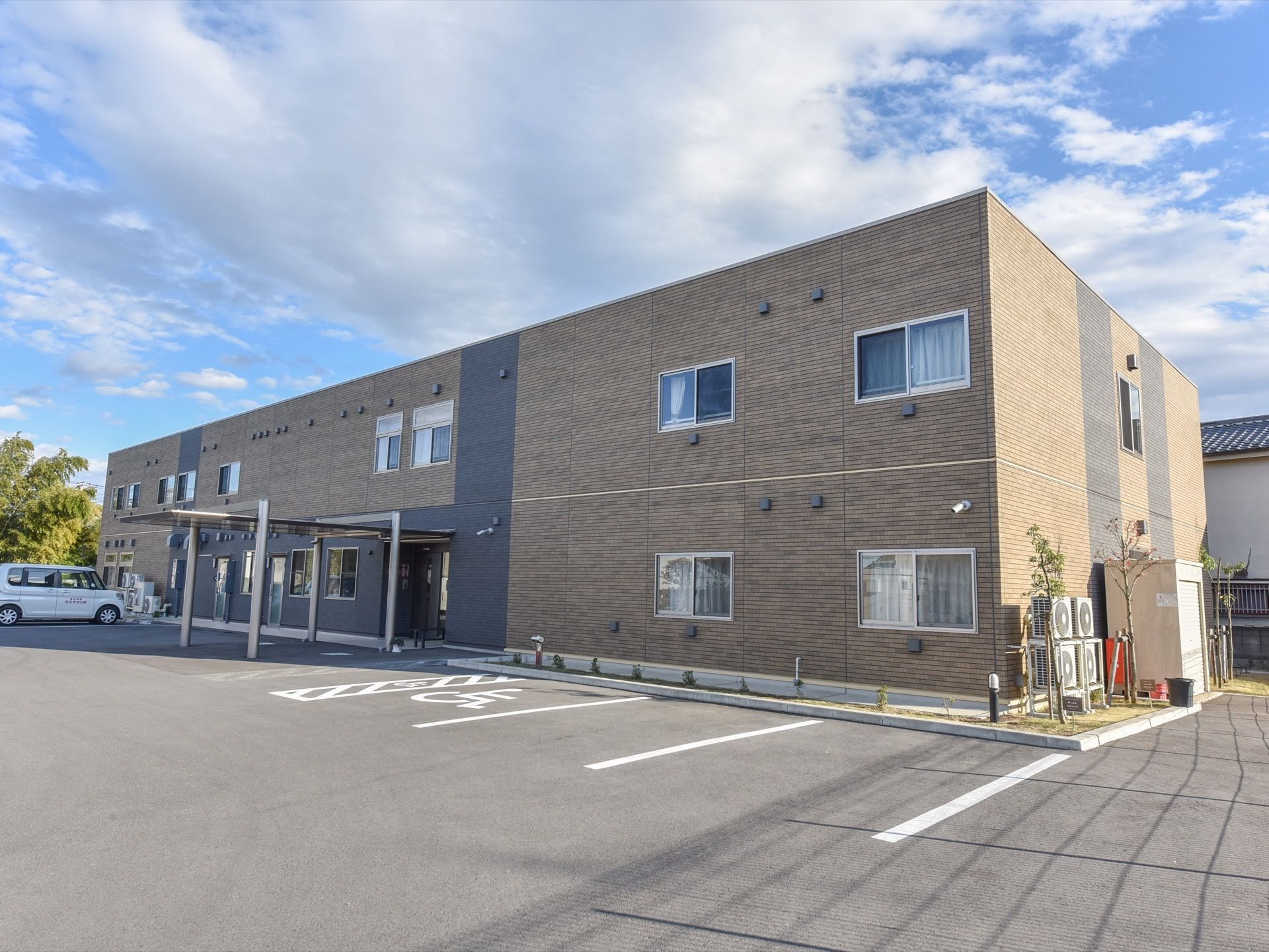 施設は落ち着いた色合いの２階建ての建物。周囲はきれいに舗装された駐車場になっている。建物に沿って花壇があり、木や花が植えられている。
