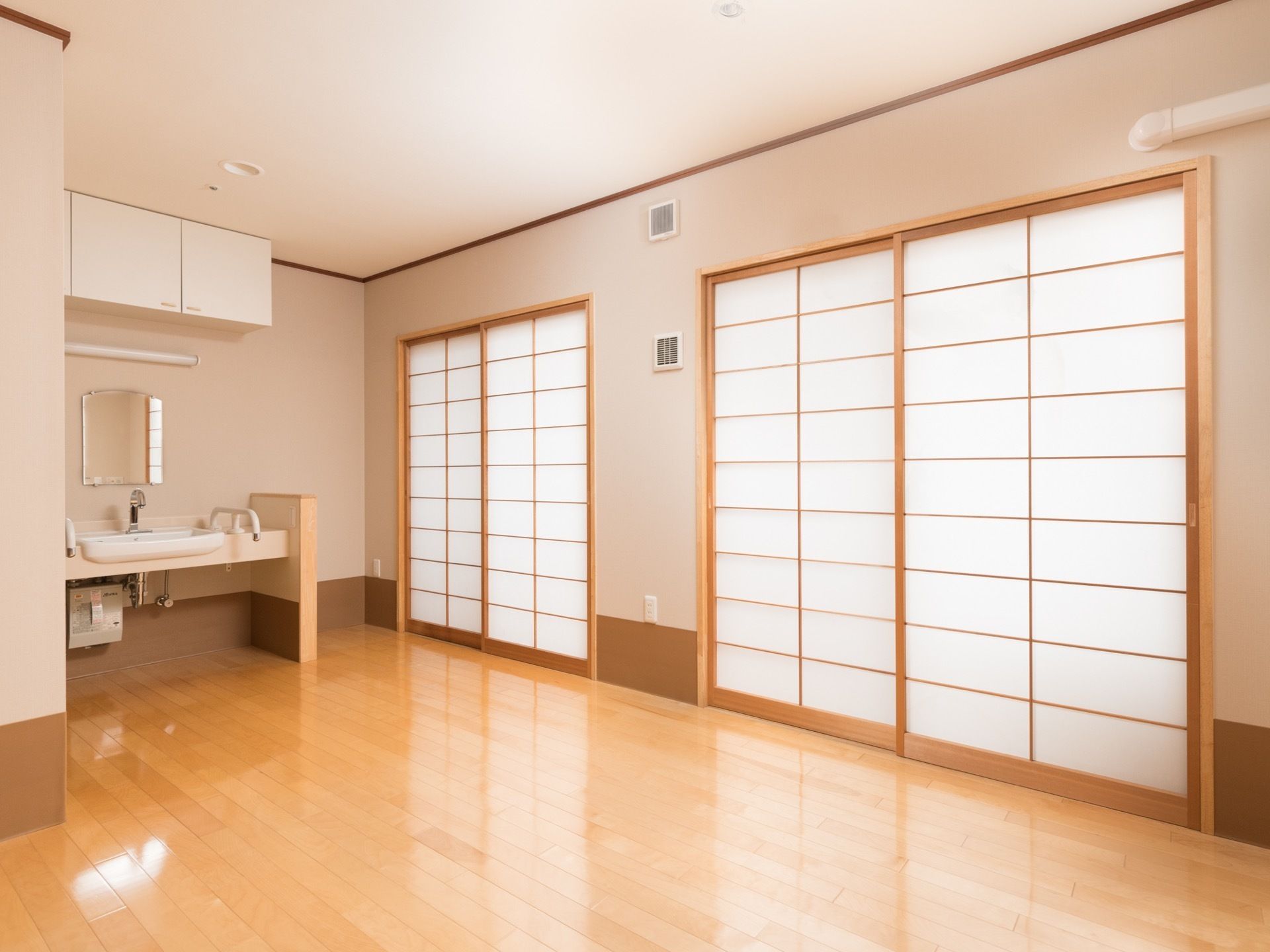 木肌色のフローリングになっている居室である。それぞれ掃出し窓が設置されており、日差しよけに障子も設置されている。