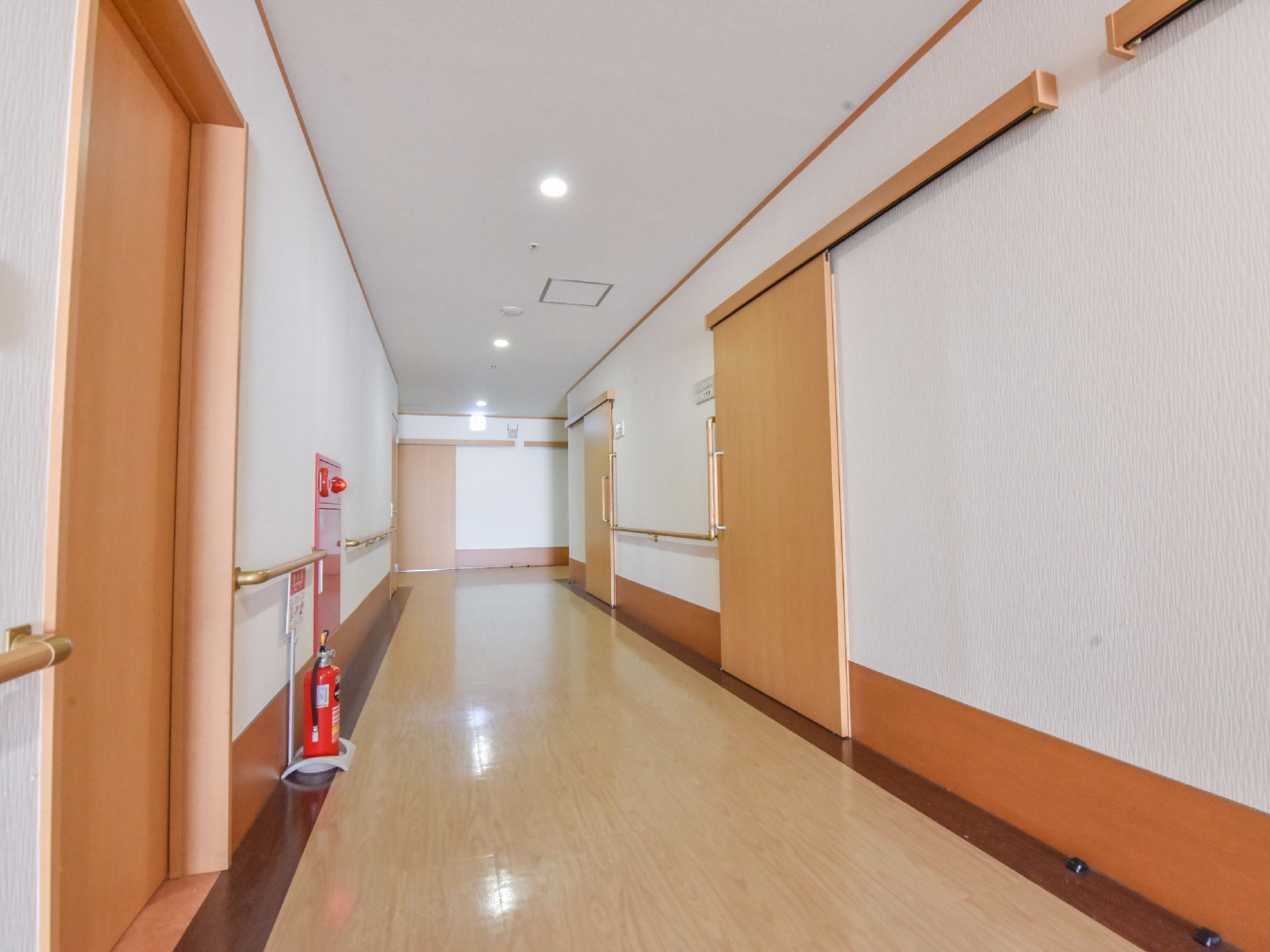 廊下に、横開きのドアがいくつか並び、手すりが取り付けられている。壁には消火栓、床には消火器が設置されている。