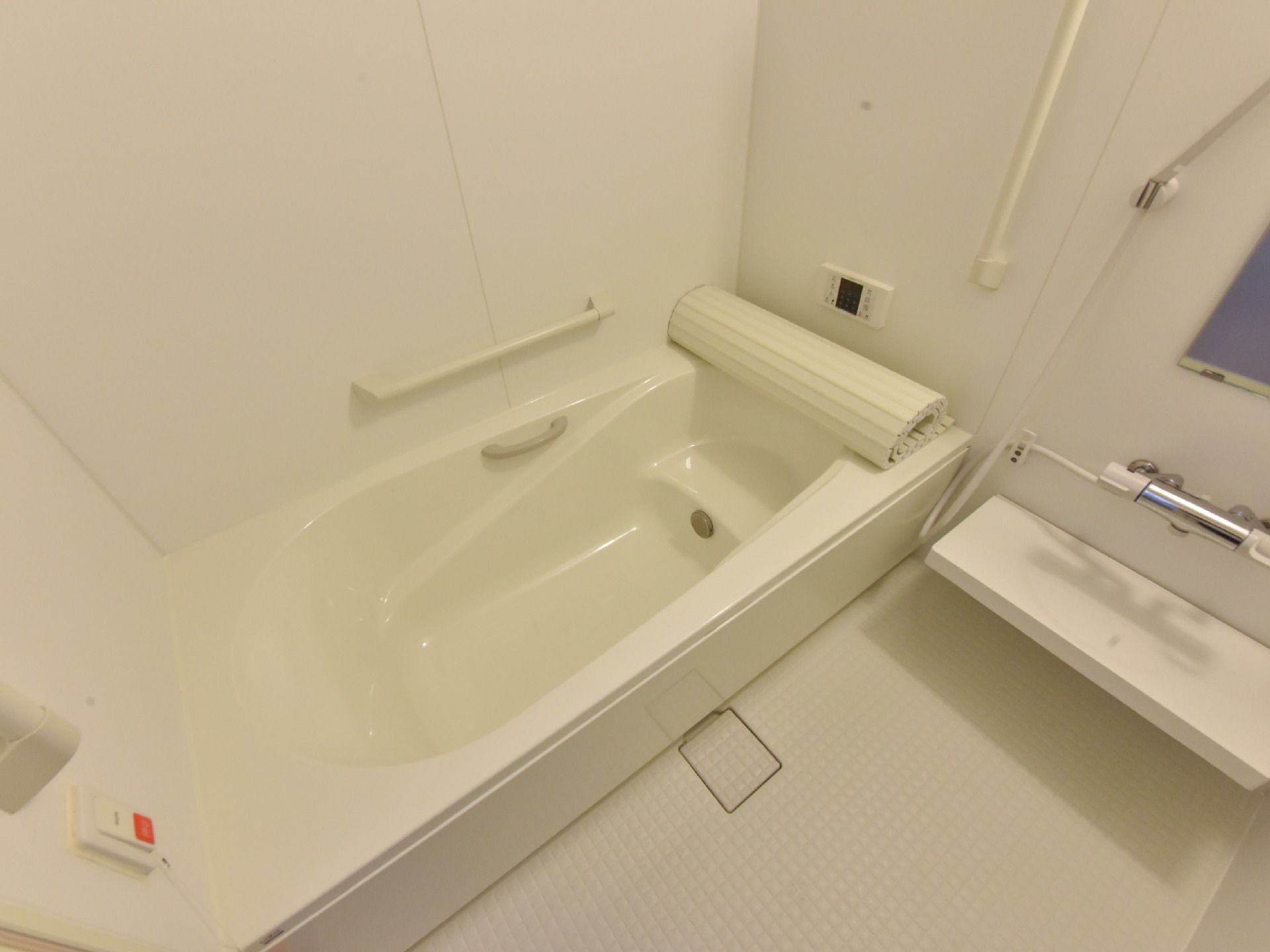 浴室の中に、浴槽とシャワーが設置されている。シャワー付近の壁に鏡がついていて、蛇口の下に備品を置く棚がある。
