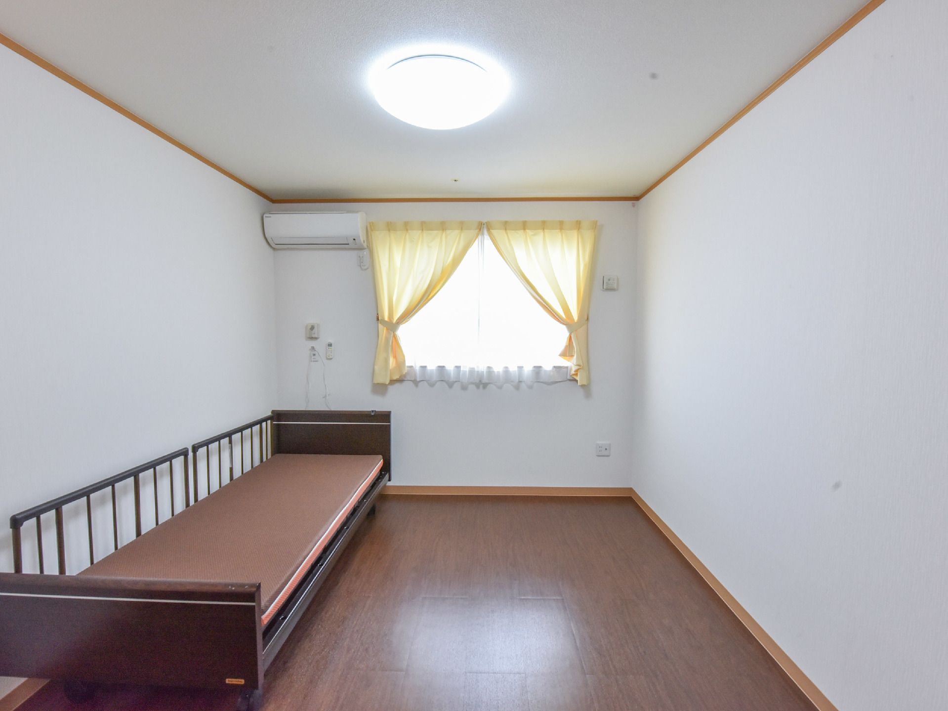窓に黄色いカーテンが付いていて、柵付きのベッドが設置されている居室