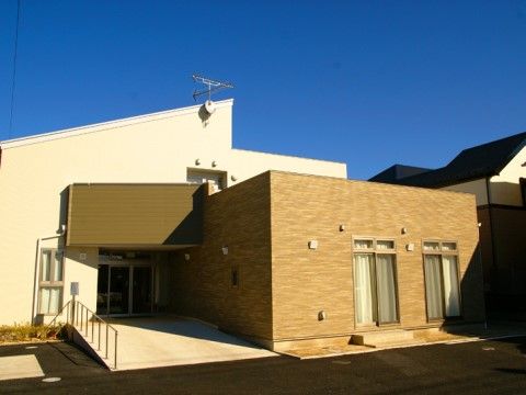 白・茶色を基調とした１階建ての明るい印象の外観である。玄関はスロープになっており、手すりも付いている。