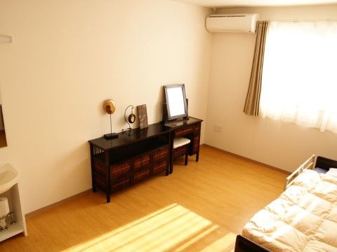 フローリングの床の居室には介護用のベッド、鏡台、洗面台、エアコンが設置されている。大きな窓から日が差し込み明るい印象である。
