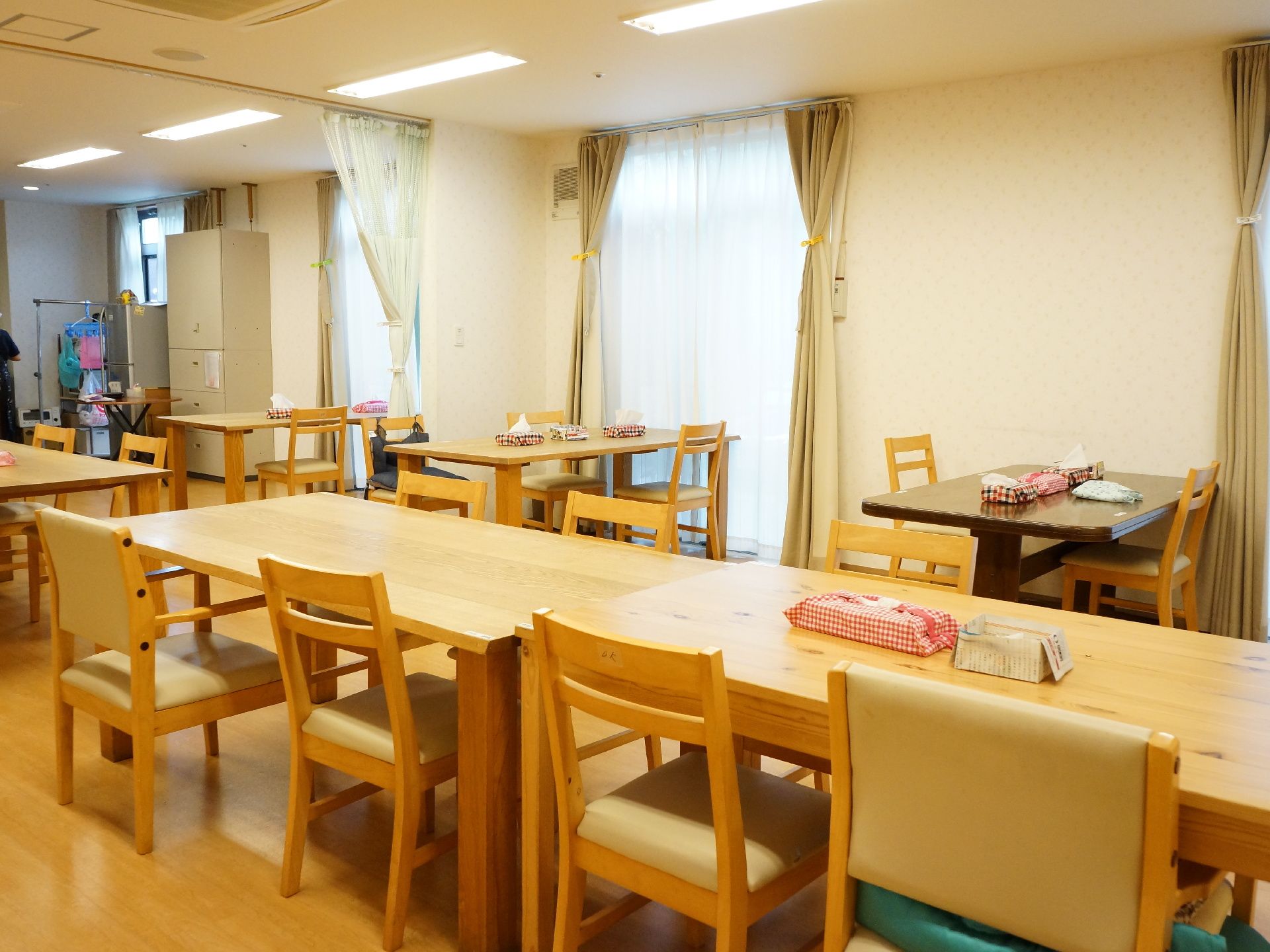 食堂には、木目調の机といすが並べられている。たくさんの数がある。カーテンの掛かった大きい窓もあり、明るい室内である。