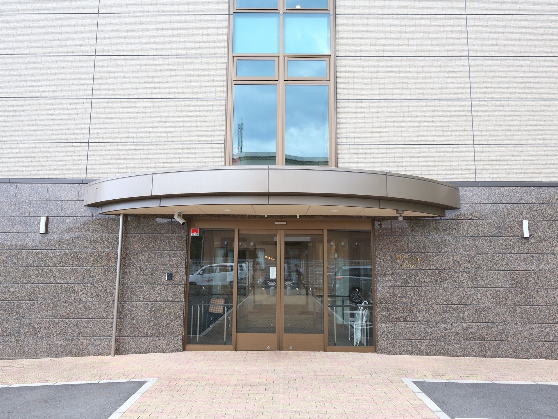 一見するとビルのような建物で、上階にはミラーガラスがはめ込まれている。玄関の上には屋根が設置されている。