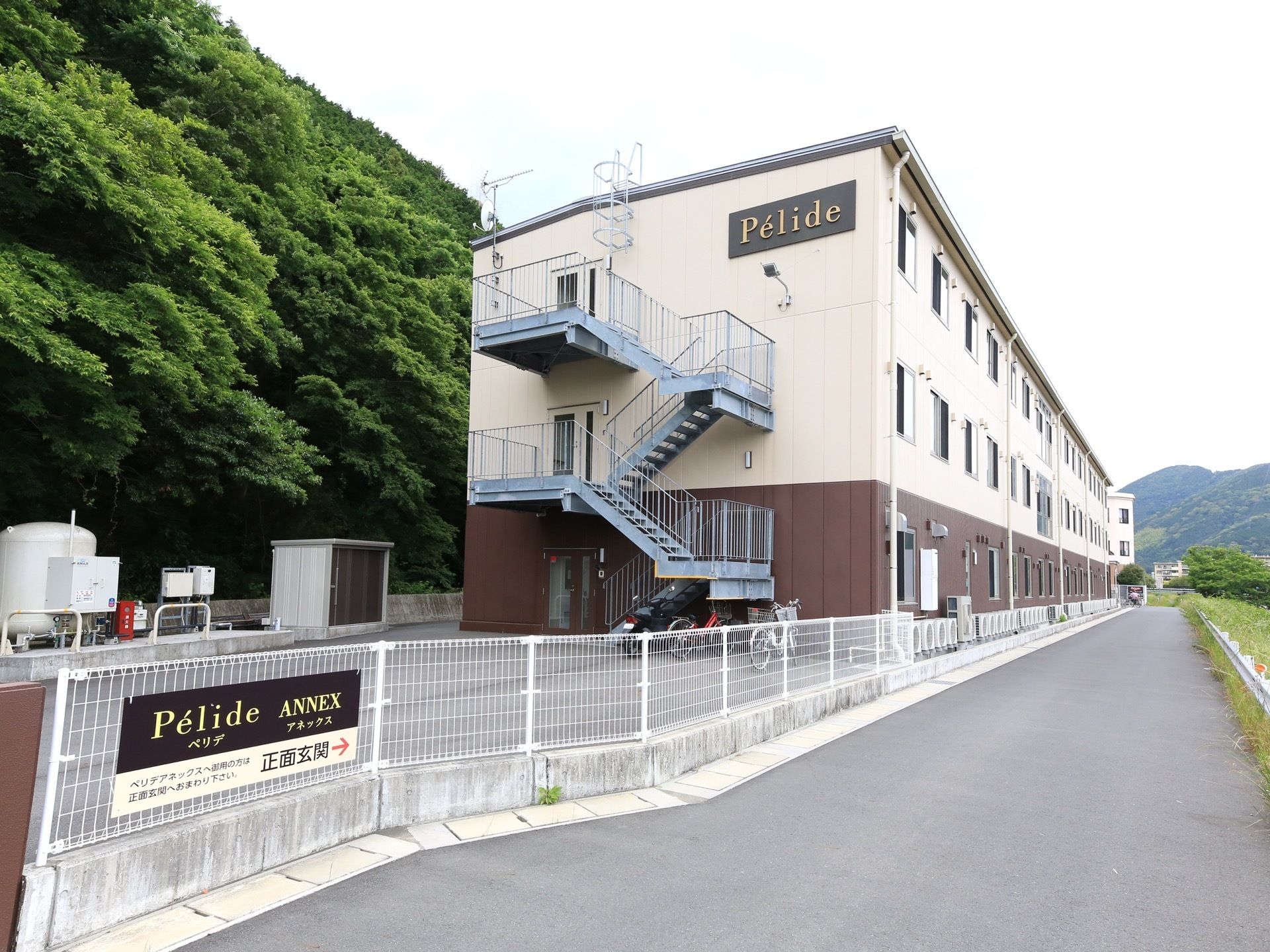 3階建てで、建物の側面に外階段が取り付けられている。階段の下には自転車が数台置いており、その近くには倉庫がある。