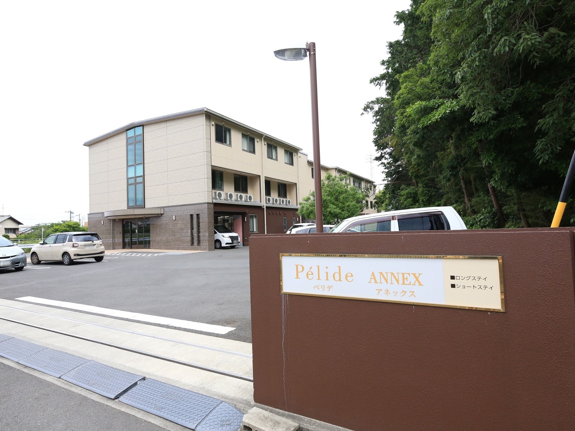 正面玄関の壁には、施設名とともにロングステイ、ショートステイと書いてある。道路と駐車場の間には、段差プレートが敷き詰めらえている。