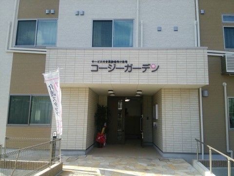 白色とブラウン系の落ち着いた色の外壁である。玄関部分に施設名が大きく表示され、遠くからでも見やすい。