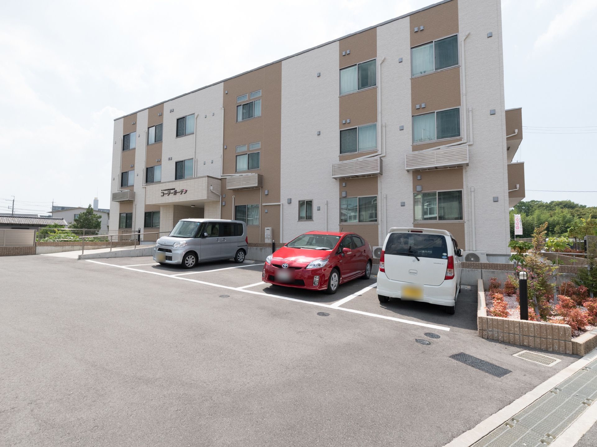 施設は3階建てになっている。敷地内には広々とした車の駐車スペースがあり、3か所に車が止められている。