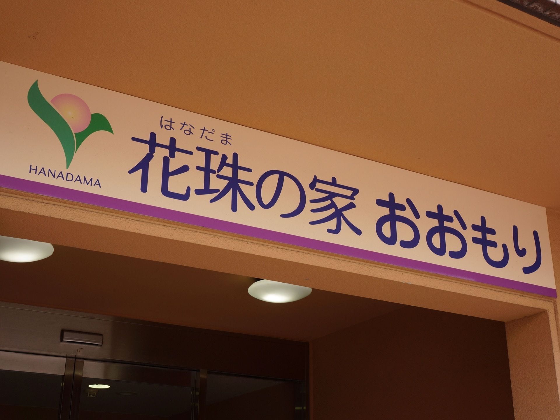 白い看板にきれいな青色の文字で施設名が書かれている。かわいらしい、花のロゴマークも書いてあり、わかりやすくなっている。