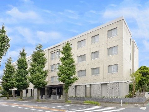 周囲に大きな木が植えられている、白塗りの外装をした施設外観
