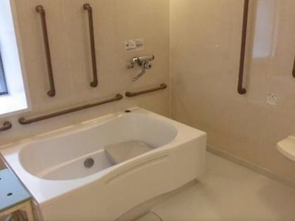 茶色の手すりが多くつけられた浴室には白い浴槽が設置されている。