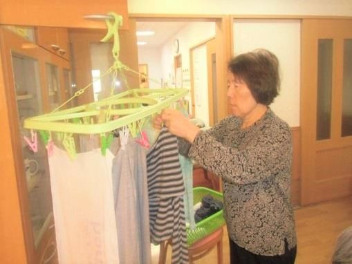 洗濯バサミに洗濯物を干している女性入居者。共有スペースで行っている。