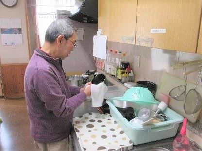 キッチンで食器を拭いている男性入居者の姿。入居者はメガネをかけている。