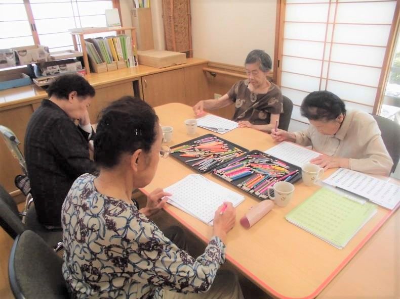 4人の女性入居者が同じテーブルにいながら、塗り絵や写経などそれぞれ好きなことを楽しんでいる。