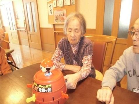 ダイニングテーブルで「黒ひげ危機一髪」を楽しむ入居者の姿。真剣な表情で女性入居者が剣を刺している。