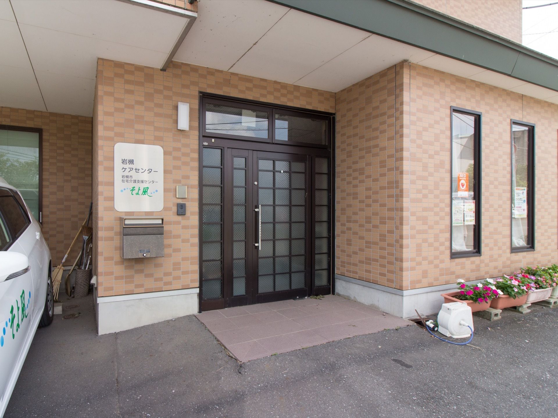 普通の一軒家のような外観の玄関である。横の壁にはポストやインターホン、施設名が書かれた表札が設置されている。