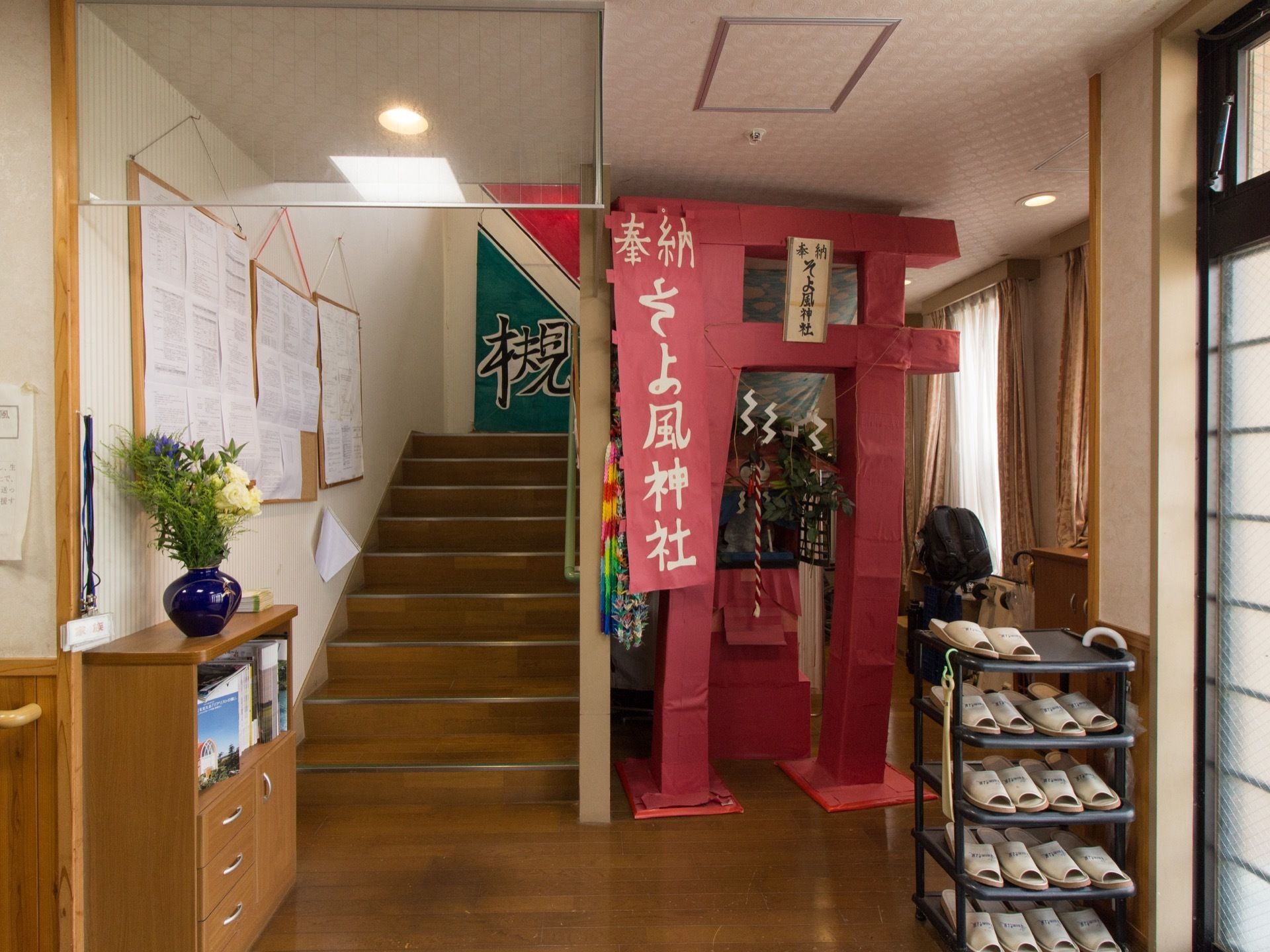 館内用のスリッパが複数ラックに入って用意されている。階段の横には手作りの本格的な神社が飾られている。