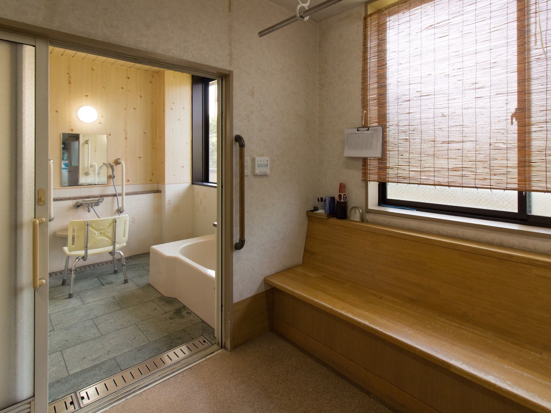 浴室の扉は曇りガラスでスライド式となっている。脱衣所の壁には椅子が設置されており、窓にすだれが掛けられている。