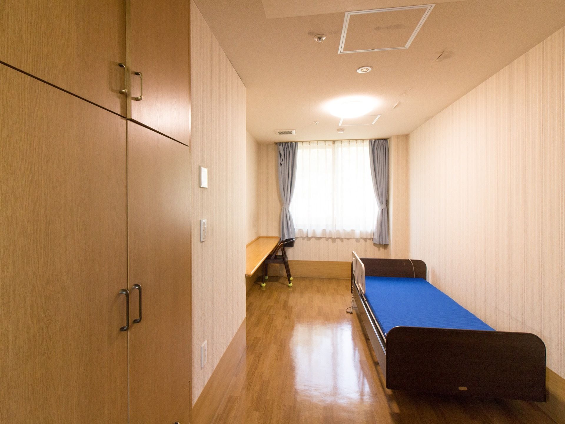 居室に備えつけられた介護ベッドには青いマットが敷かれており、転落防止のための柵が取りつけられている。