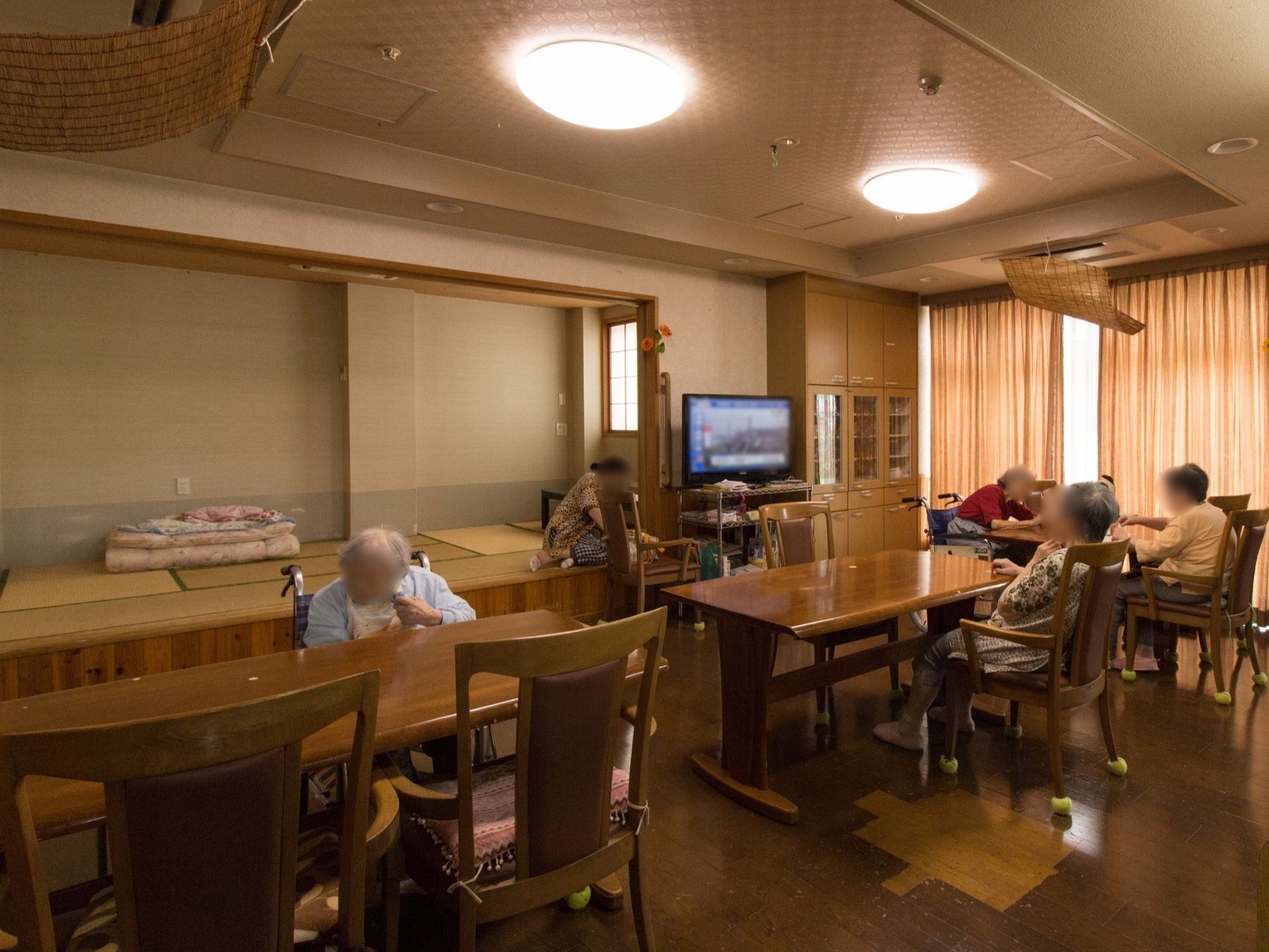 テレビが設置されたリビングで入居者様が思い思いの時間を過ごしている。奥には畳スペースが設けられている。