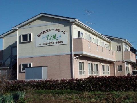 建物の側面に大きな看板があり、施設名が緑色の文字で描いてある。１階と２階のベランダの壁はピンク色に塗ってある。