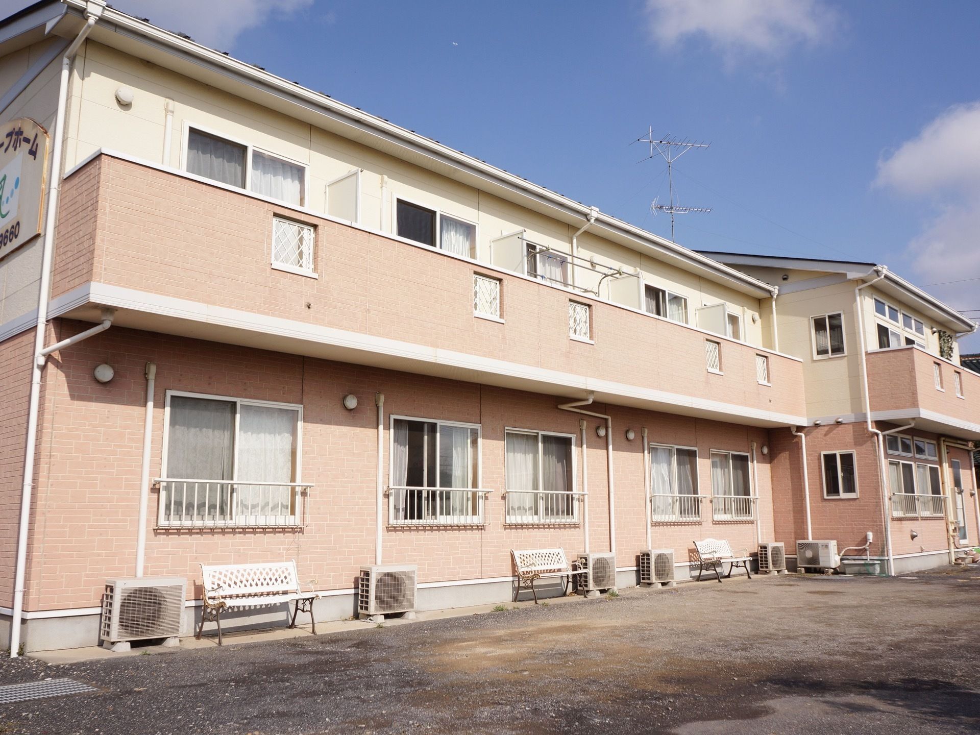 グループホームは２階建ての建物になっている。また２階にはバルコニーがあり、１階にはベンチが置かれている。