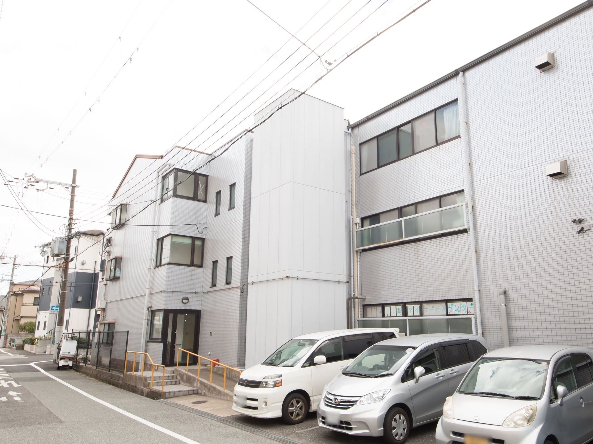 施設は３階建ての白い建物である。建物前に駐車スペースが設けられており、手すり付きのスロープと階段がエントランスに設置されている。
