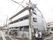 道路の角地に建つ、３階建ての建物である。玄関のある面に駐車スペースがあり、もう一方の面に自転車置き場がある。
