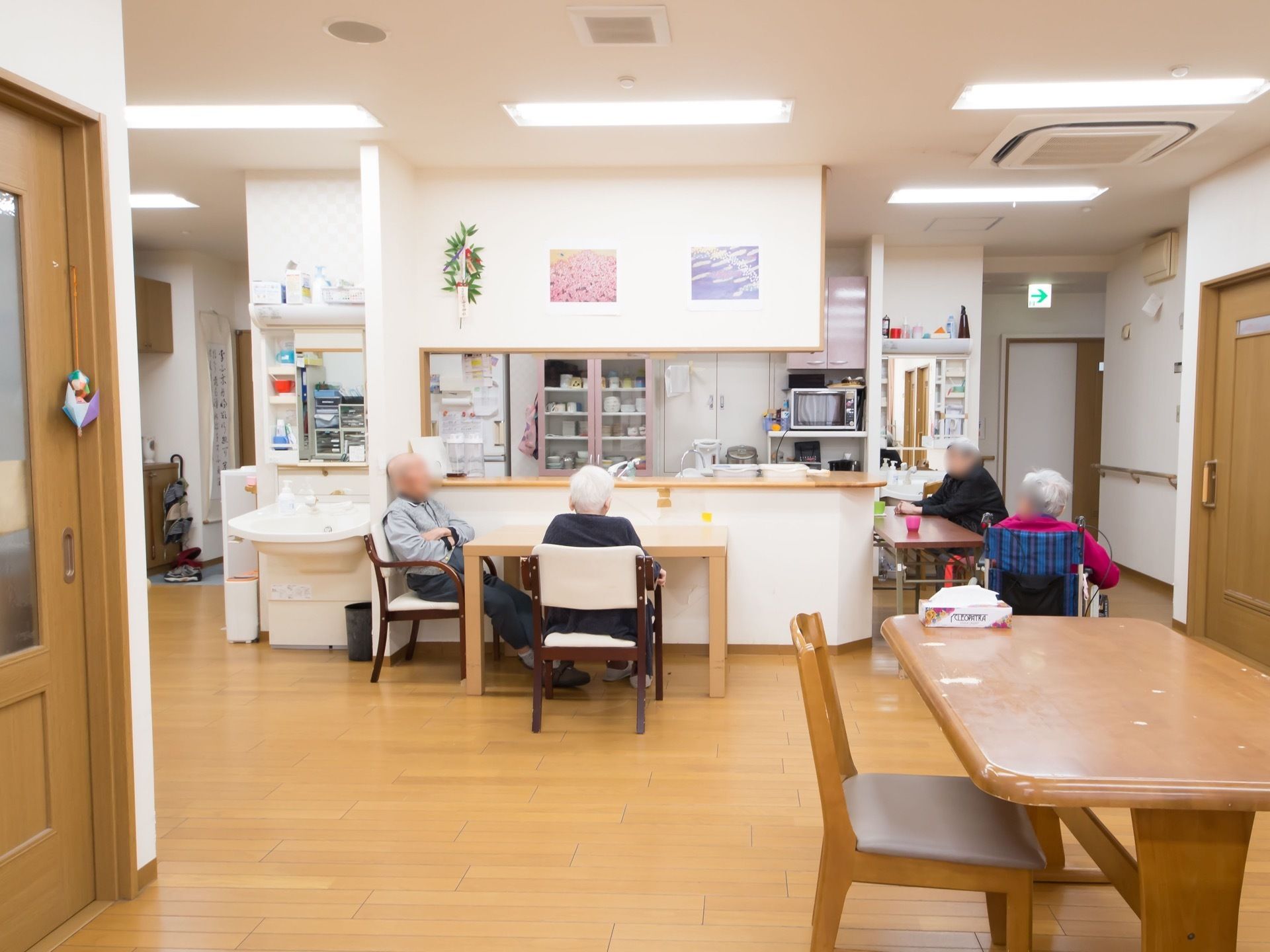 キッチンカウンターの隣に洗面台が設置されている。数名の入居者様がカウンター周りに置かれたテーブルに着いている。