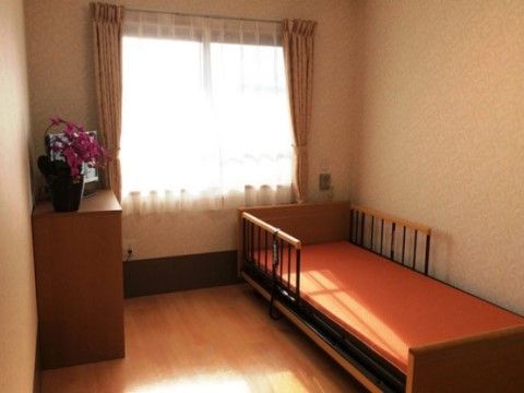 介護用ベッド、テレビ、お花が置かれた居室である。プライベートな空間が確保されており、すべての居室にエアコンも完備。