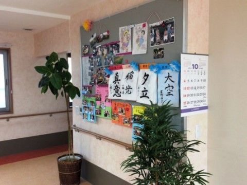 通路にはイベント時の写真や入居者様の作品などが飾られた掲示板がある。壁には手すりが付いており、移動も安心である。