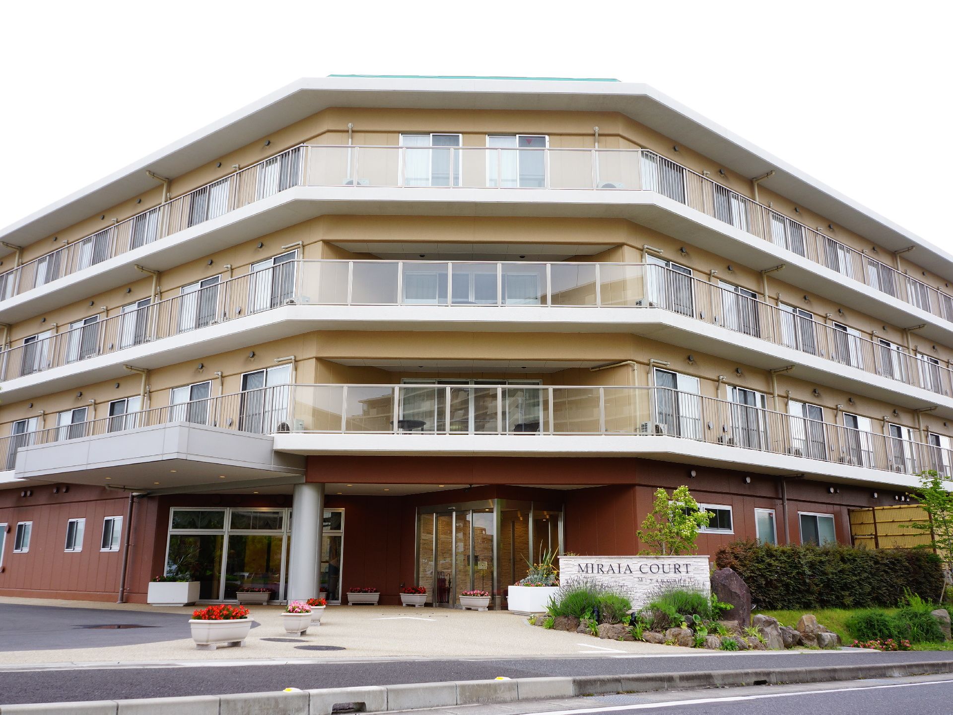 4階建の建物で窓とテラスが多い。入り口は奥まっており雨に濡れずに送迎ができるようになっている。周辺に草木が植えられている。