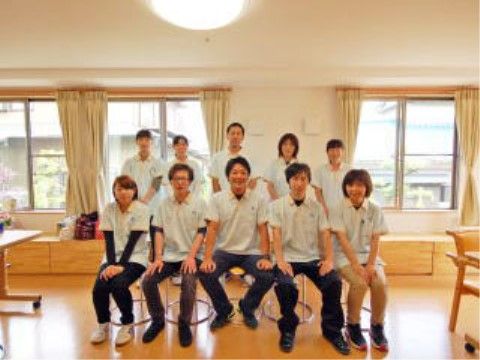 明るい部屋の中で、笑顔を見せて二列に並んでいる十名のスタッフ