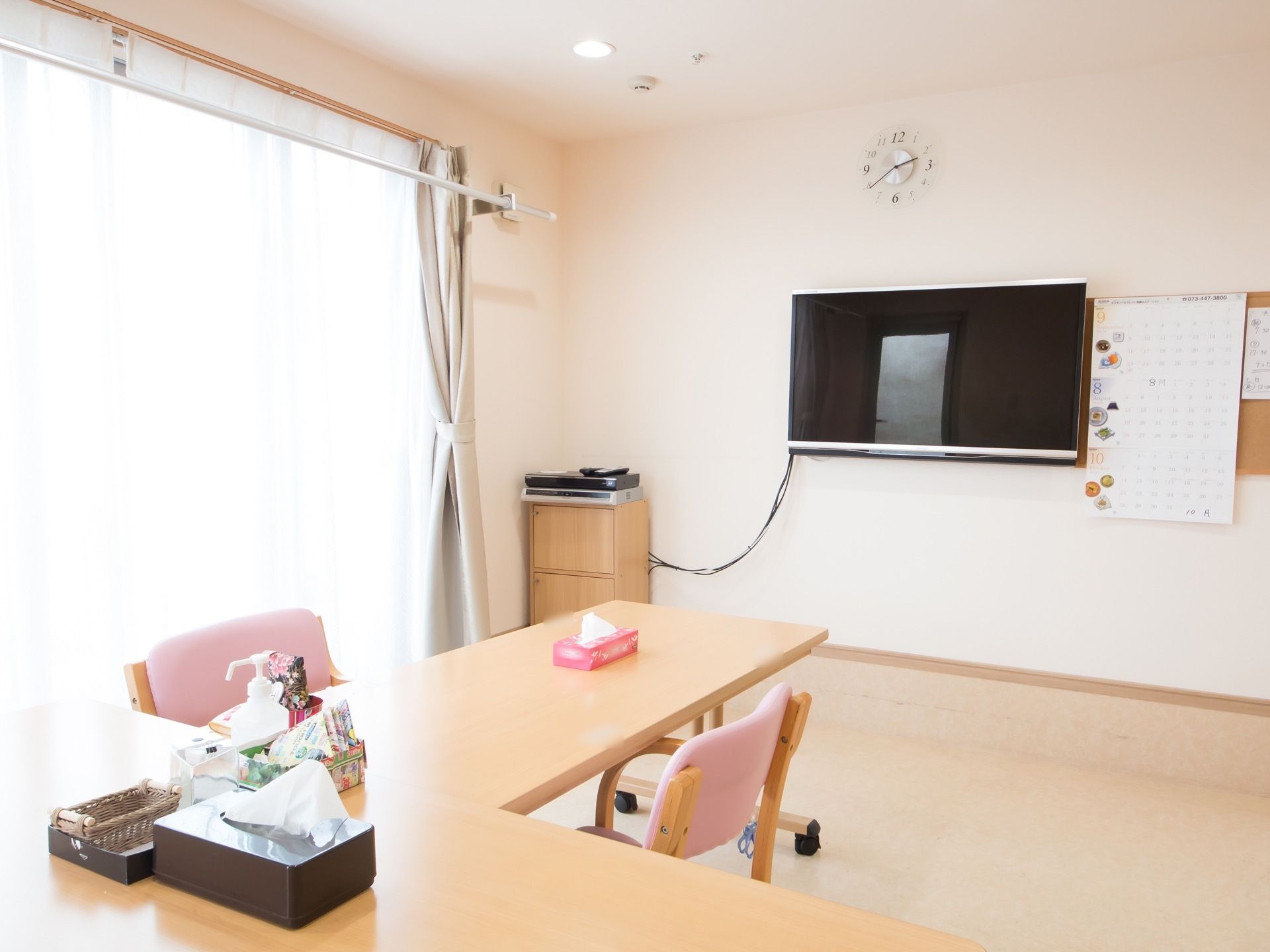 窓からの光で明るい部屋にＬ字型に組まれたテーブルがあり、椅子がセットされている。壁にはテレビがあり、ビデオ機器と接続されている。