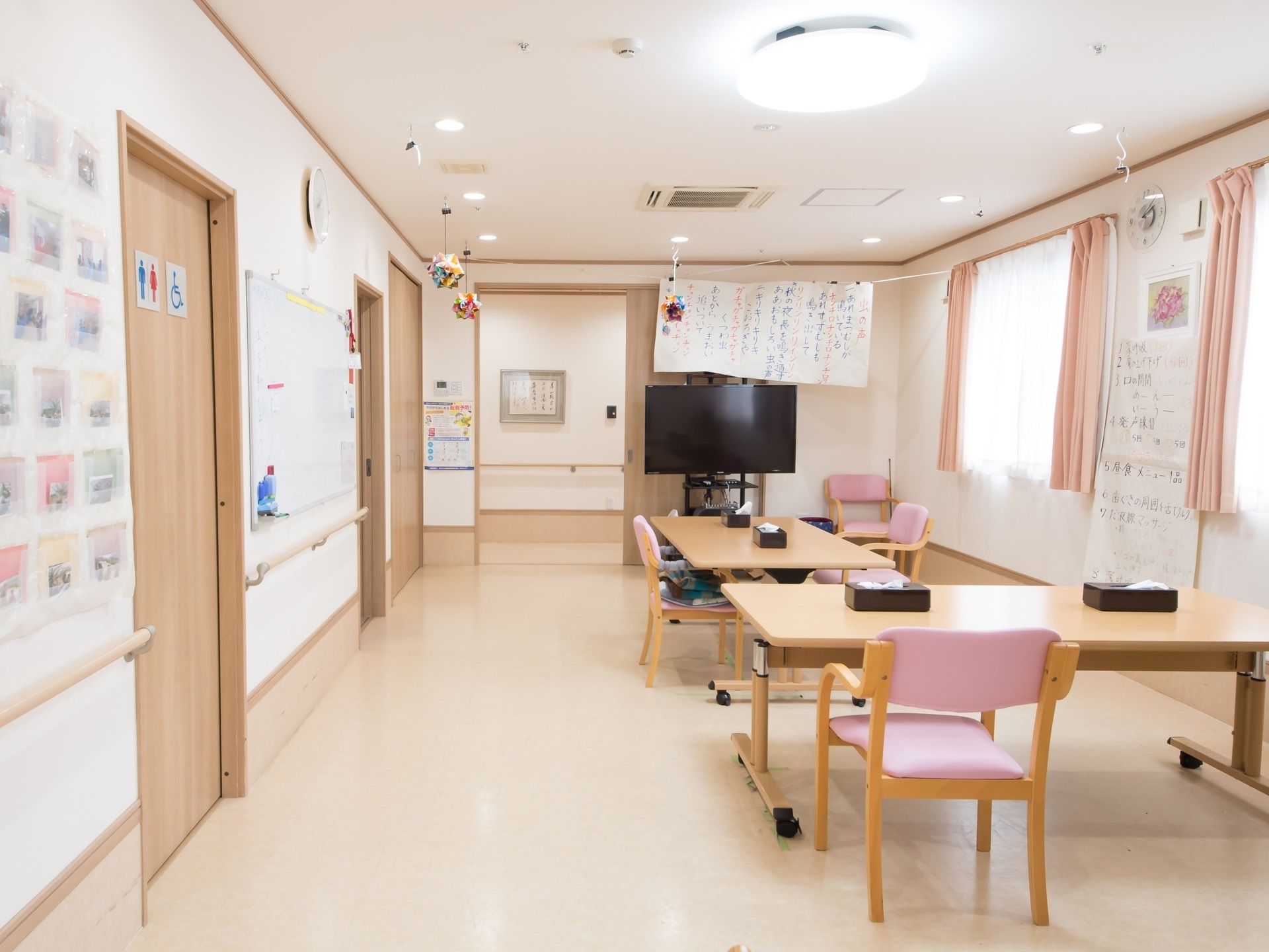 広い部屋にピンクの背もたれを持つ椅子とテーブルが置かれている。奥にはテレビがあり、大きな文字で歌詞を書いた紙が下げられている。