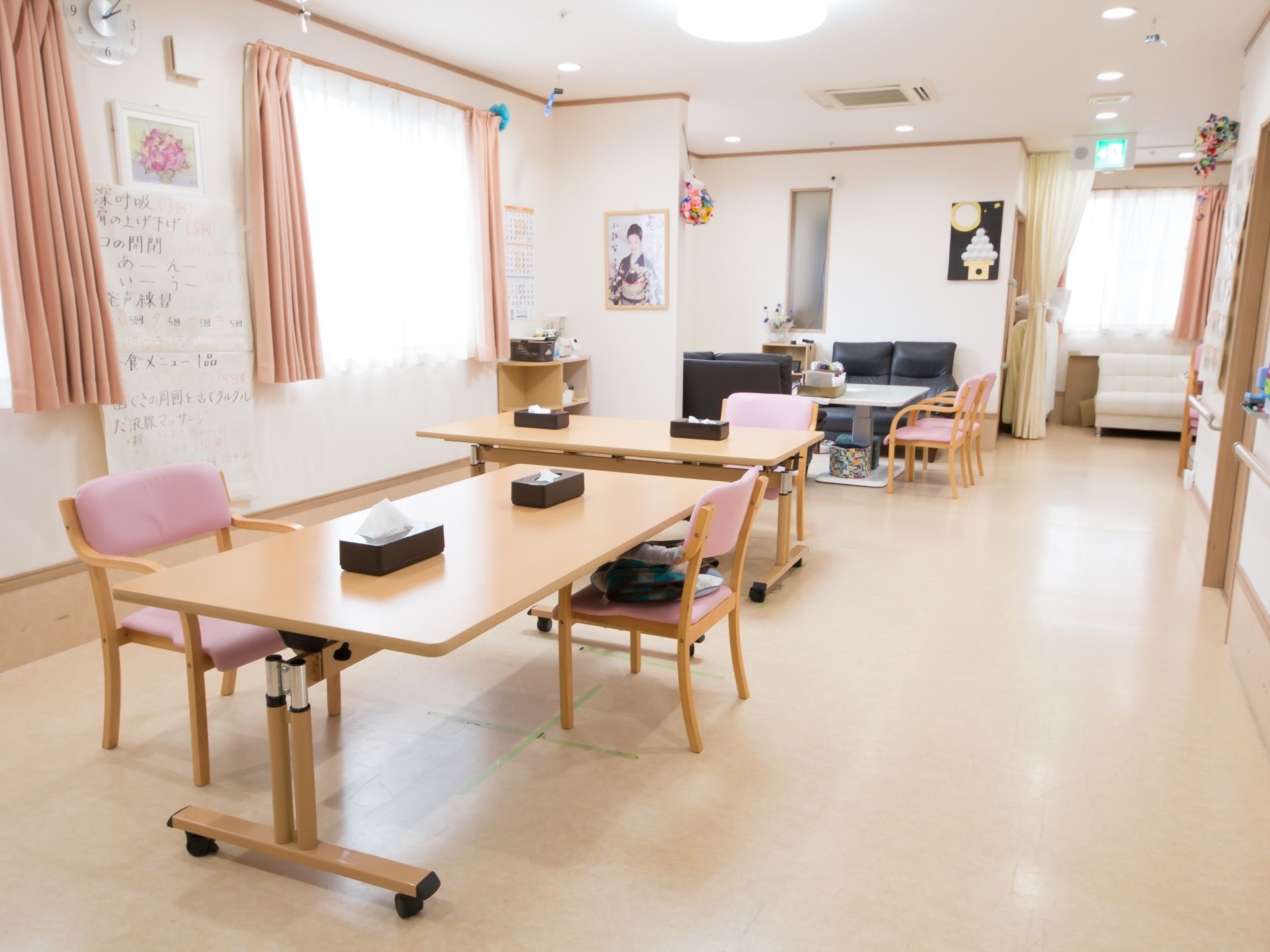 広くて明るい部屋に、テーブルと椅子がセットされている。奥にソファなどの置かれた談話室が見える。窓にはピンクのカーテンがかかっている。
