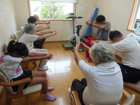 椅子に座り、スタッフや子供と一緒に体操をしている入居者たち