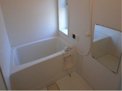 白を基調とした浴室。小窓が付いていてその横には給湯器のボタンが取り付けられている。洗い場には鏡がある。