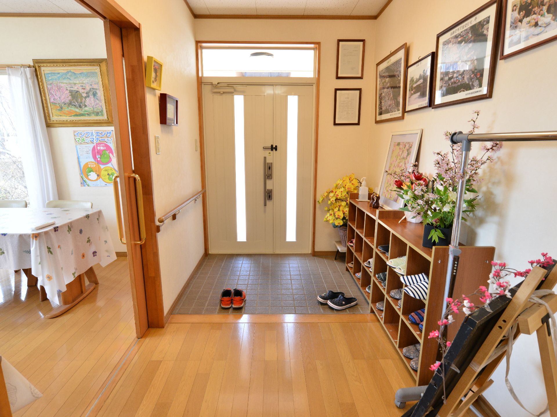 玄関に向かって左手に手すりがあり、向かい側は下駄箱になっている。壁や棚には額装した写真や花が飾られている