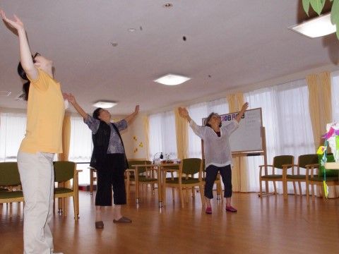 テーブルセットが置かれた部屋の一角で、立ちながら体操をしている三名の入居者