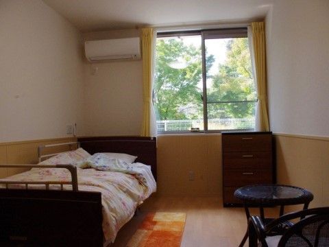 お部屋はゆったりとした広さがあり、窓からは緑が望むことができる。室内には、ベッドやテーブルなど家具が設置されている。