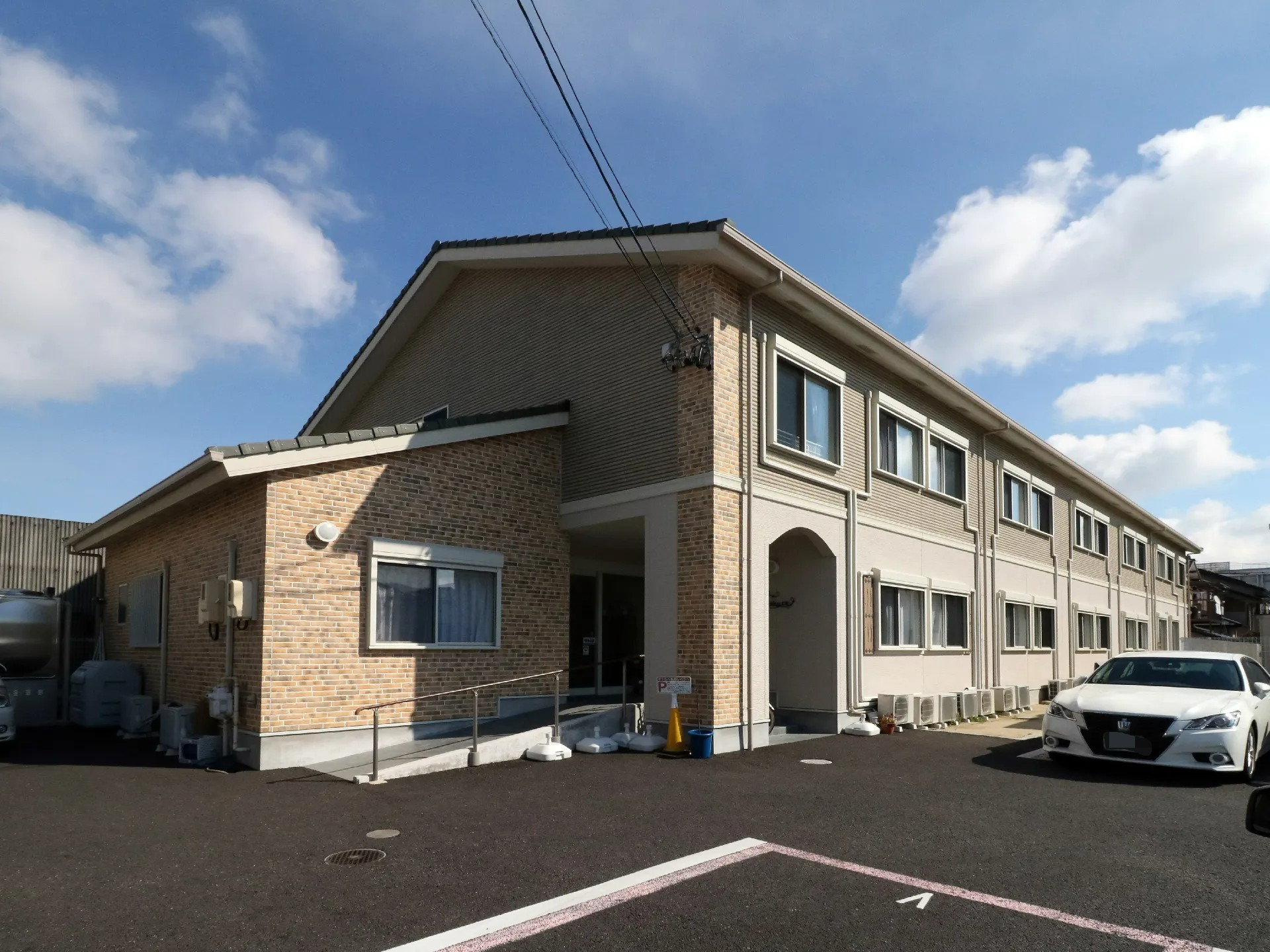 壁面の一部にレンガ調の模様があり細長い形状で入り口にむかって手すり付きのなだらかなスロープがある。駐車場と隣接している。