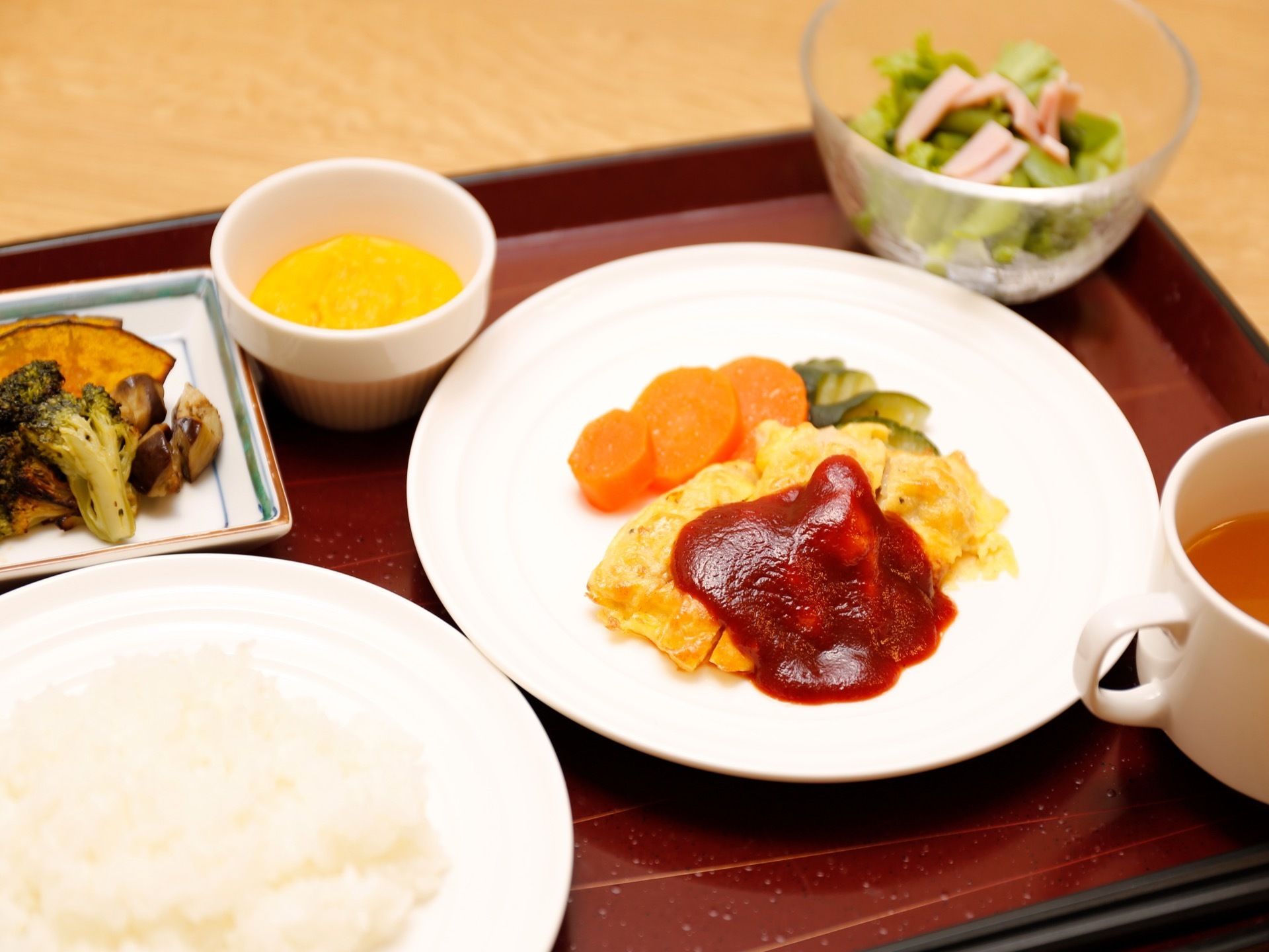 施設では入居者様の日々の食事が提供されている。メインの皿にはケチャップの掛かったオムレツが乗っている。