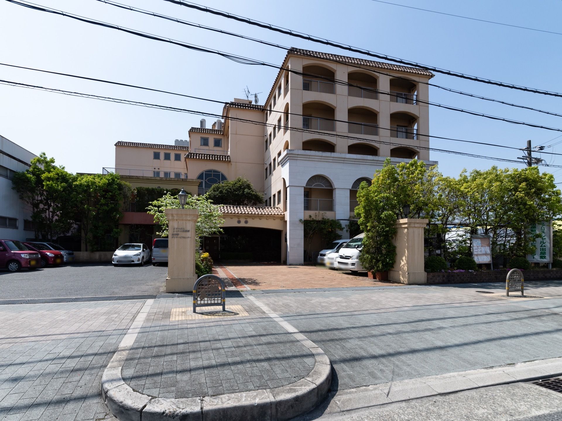 ベージュ色の壁で洋館のような雰囲気である。門の右側に施設名が書かれた看板がある。敷地内に駐車場が完備されている。