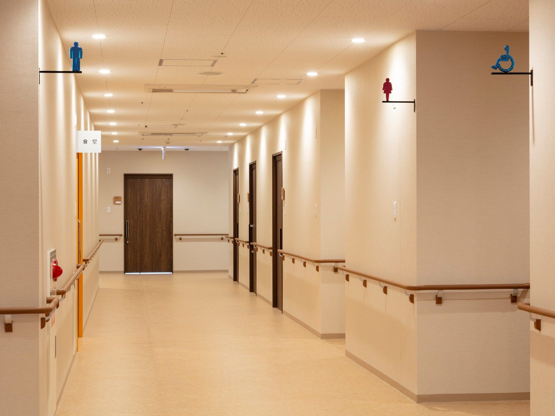 広めの廊下に手すりが取り付けてある様子。両側に個室が並んでいる建物内の様子が分かる
