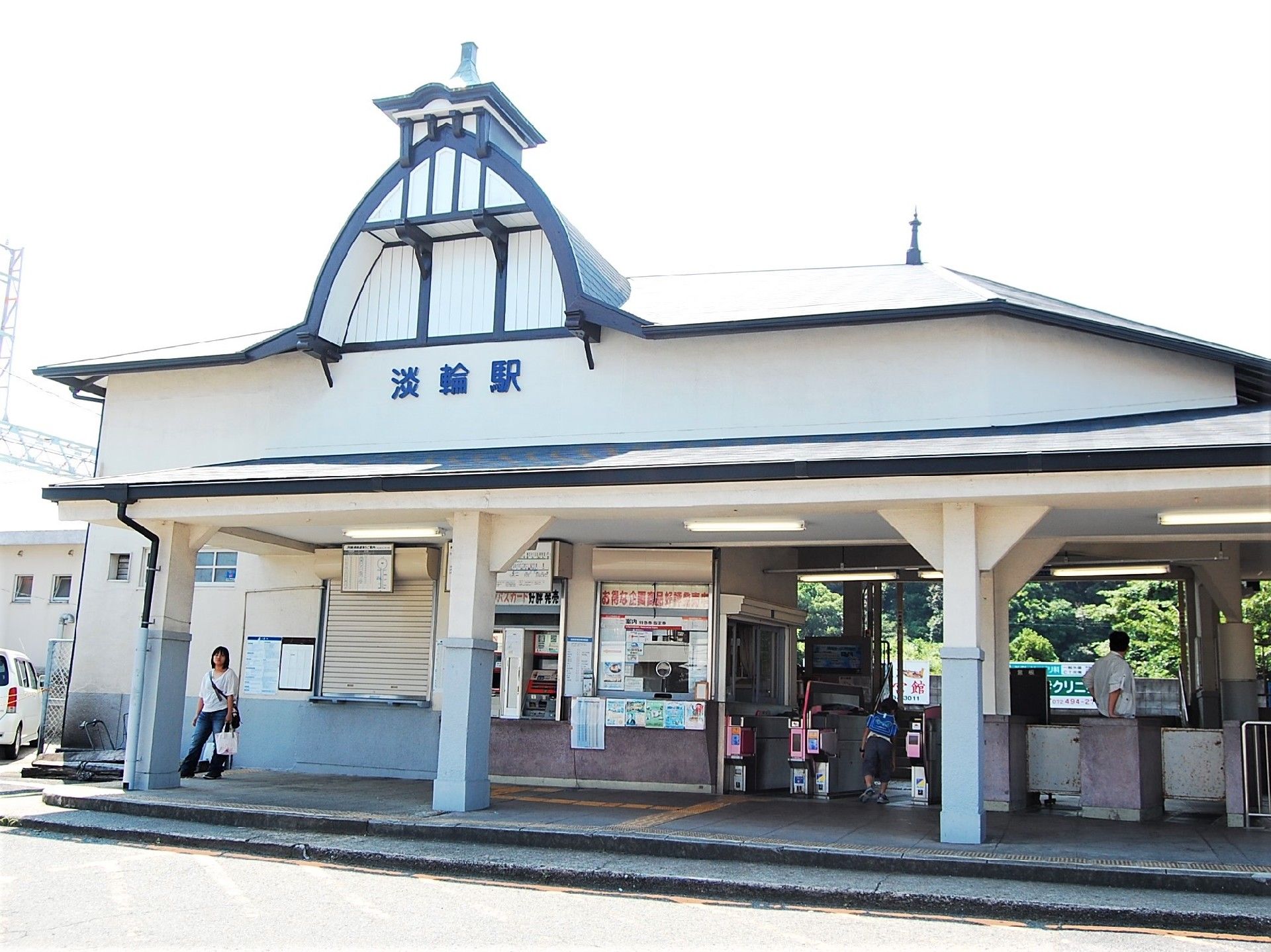 白い外観の駅舎がある。青い文字で駅名が書かれている。改札口近くの床には、黄色い点字ブロックが敷かれている。