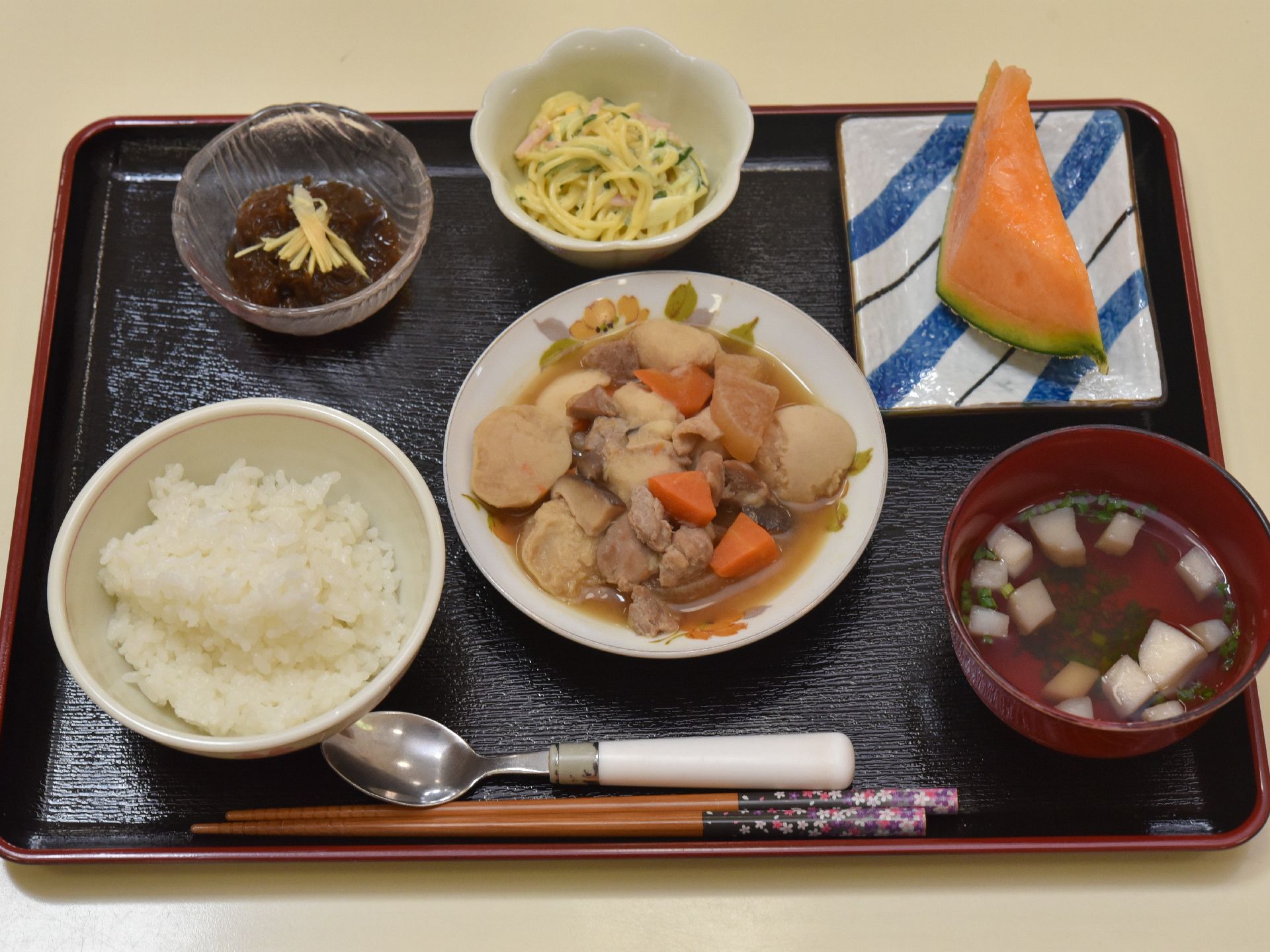 里芋や大根、人参、鶏肉の煮物、スパゲティサラダ、もずく、デザートのメロン等、栄養のバランスを考えた献立が並んでいる。