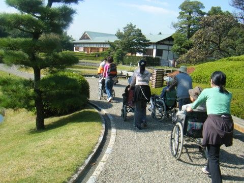 スタッフたちに車椅子を押されながら、青空の下で散歩をする入居者たち